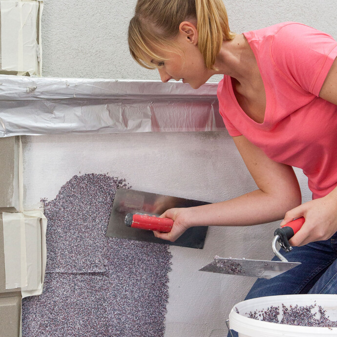 Frau zieht Mosaikputz mit Glättkelle auf.