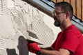 Un bricoleur applique l'enduit à la truelle sur une façade ; instruction étape par étape pour la rénovation et la remise en état de l'enduit Baumit.
