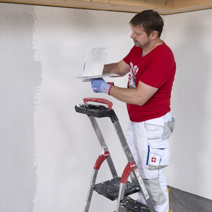 Person streift Reibebrett an Glättkelle ab, um überflüssiges Bindemittel zu entfernen.