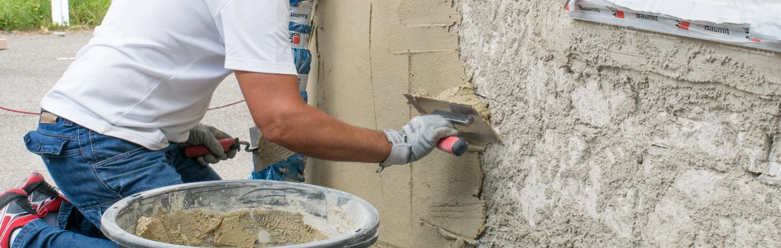 Handwerker tr&auml;gt Putz an Au&szlig;enwand auf; Baumit-Produkte f&uuml;r effektive Fassadenrenovierung.