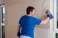 Heimwerker glättet Innenputz einer Wand mit Kelle für einen gleichmäßigen Abschluss.
