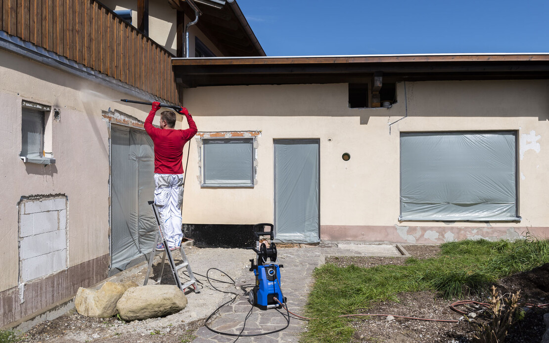 Heimwerker steht auf einer Leiter und reinigt die Fassade mit einem Hochdruckreiniger.