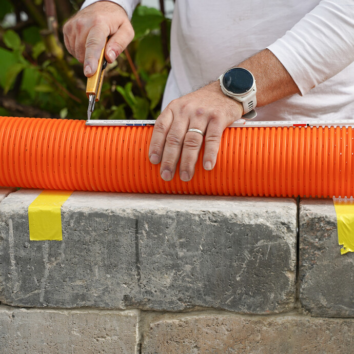 Detailfoto: Drainagerohr wird auf die benötigte Länge mit einem Cuttermesser gekürzt. Die Rohre sind aus Kunststoff und lassen sich einfach zuschneiden.