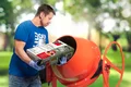 Heimwerker füllt Zementmischer mit Baumit-AllIn-Beton auf grünem Hintergrund.