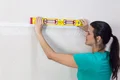 Heimwerkerin richtet mit einer Wasserwaage ein Gitternetz auf einer Wand aus, Schritt zur Wandvorbereitung für den Innenausbau.