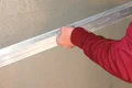 Une main passe une règle de tirage sur de l'enduit fraîchement appliqué sur une surface murale.