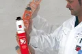Un homme en tenue de travail tient une bombe de mousse de construction devant un mur gris, prêt à réaliser l’application dans le cadre d’un projet de bricolage.