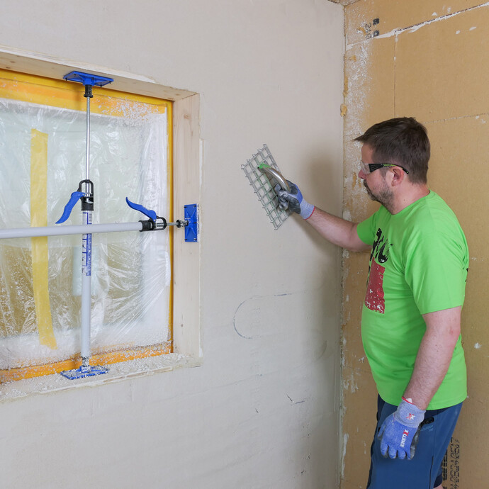 Mann reibt die verputzte Wand mit einem Giterrabott ab.