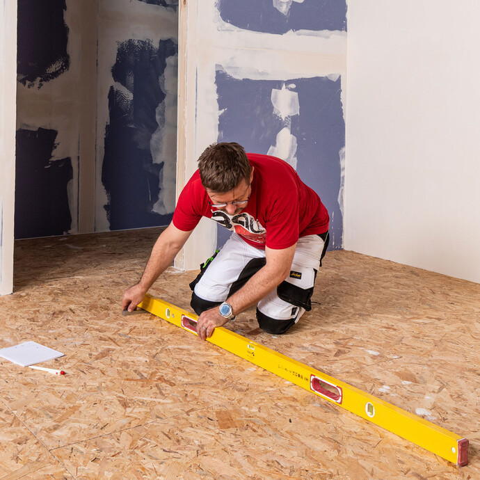 Le sol en bois est contrôlé à l'aide d'un long niveau à bulle pour vérifier qu'il n'y a pas d'irrégularités.