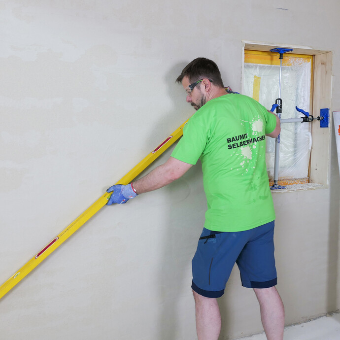 Mit einer langen Wasserwaage wird geprüft, ob die verputzte Wandfläche lot- und fluchtgerecht ist. So vermeidet man Unebenheiten.