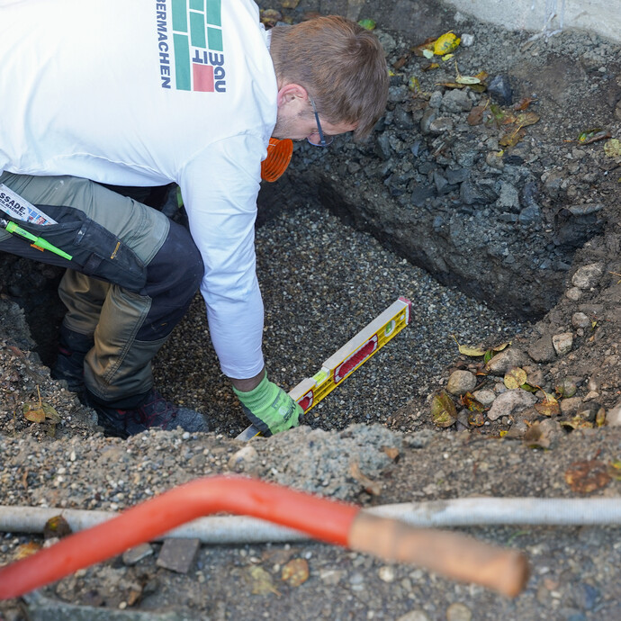 Heimwerker zieht das Kiesbett für die Sickerbox eben mit der Wasserwaage ab.