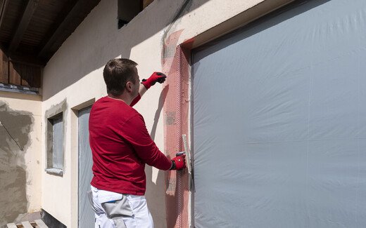 Mann positioniert die Gewebeeckwinkel mit der Gewebefahne in der Laibung der Terrassentüre.