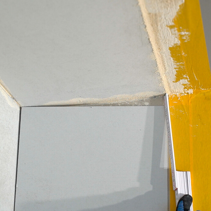 Mit einem Meterstab wird das Maß ermittelt, sodass der Anschlusskeil an der Wand bündig zur Decke zugeschnitten werden kann.