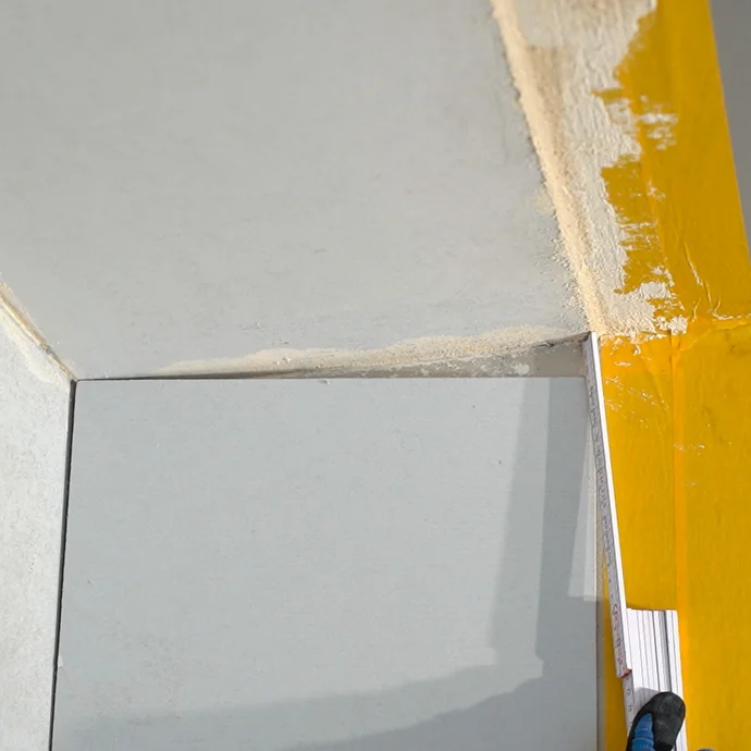 Mit einem Meterstab wird das Mass ermittelt, sodass der Anschlusskeil an der Wand bündig zur Decke zugeschnitten werden kann.