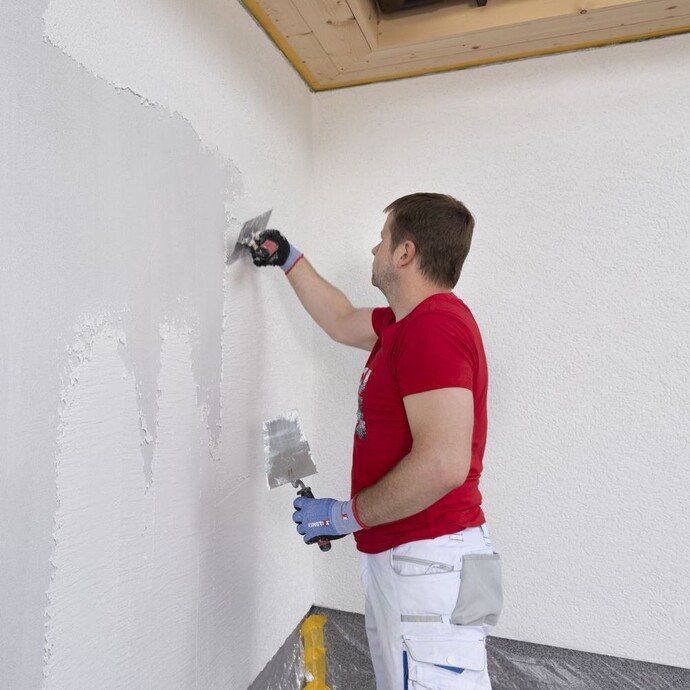 Strukturputz wird an der Wand mit einem Spachtel aufgetragen.