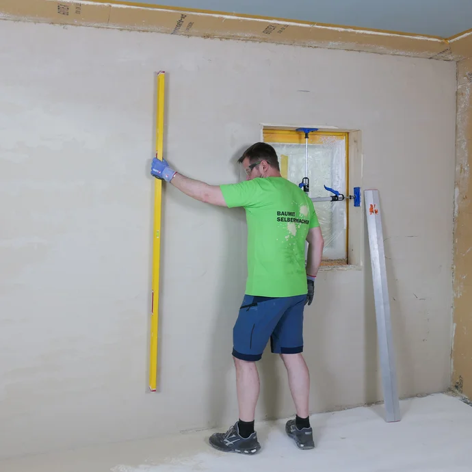 Die frisch verputzte Wand wird mit einer langen Wasserwaage geprüft, falls es noch unebene Stellen an der Wand gibt.