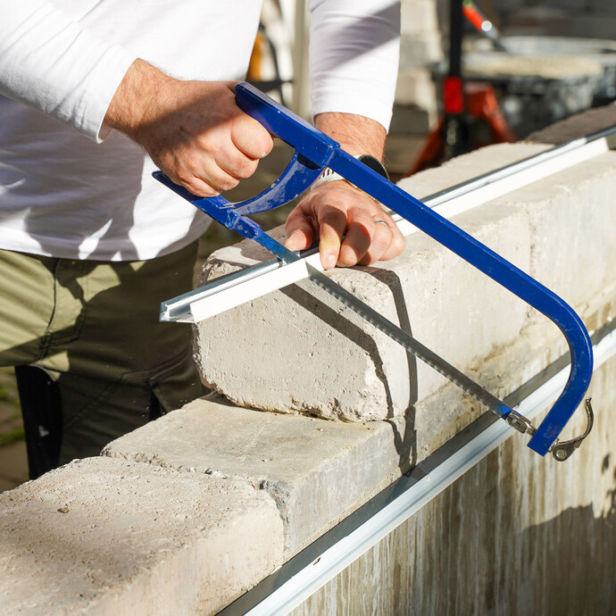 Handwerker sägt mit einer blauen Eisensäge ein Abschlussprofil auf der Mauer auf die richtige Länge zu.