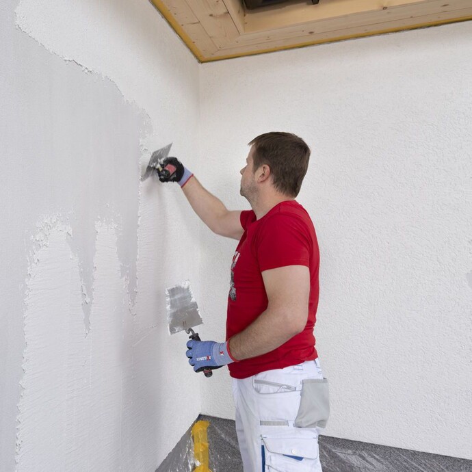 Person trägt Rillenputz in Bahnen auf Fassade auf.