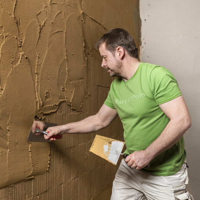 Lehmputz mit einer Glättkelle auf die Wand innen auftragen