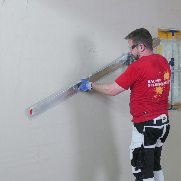 Heimwerker zieht den frisch Putz mit einer langen Kartätsche ab. 