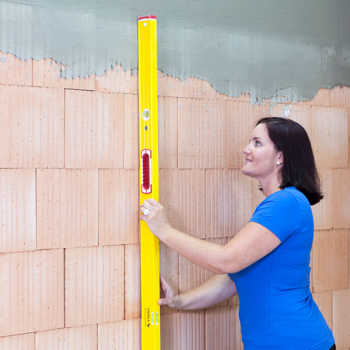 Madame vérifie que le mur n'est pas inégal à l'aide d'un long niveau à bulle.