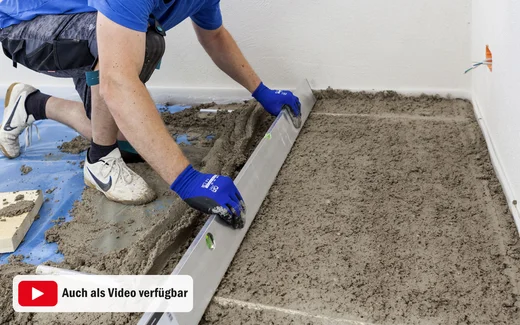 Heimwerker glättet Betonboden mit einer Abziehlatte für ein gleichmäßiges Ergebnis beim Estrich-Gießen.