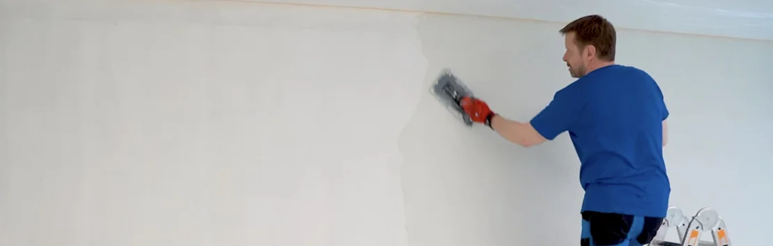 Un homme peint un mur dans une teinte claire à l’aide d’un rouleau de peinture, projet de bricolage pour l’aménagement intérieur.