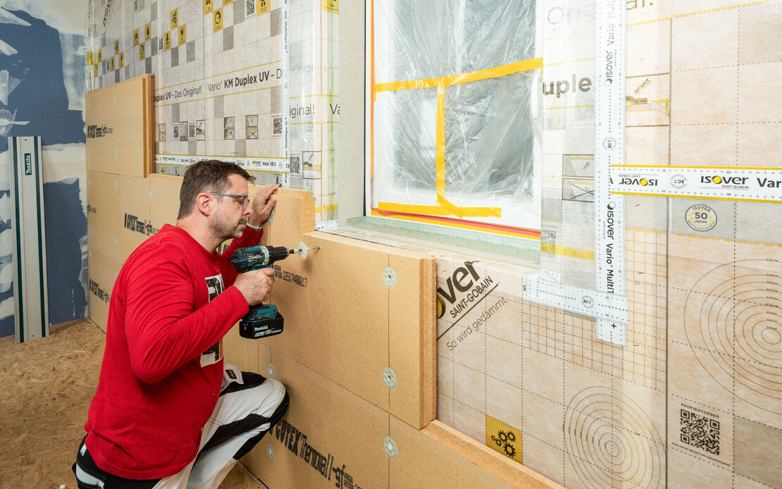 Heimwerker verschraubt Holzfaserd&auml;mmplatten im Bereich eines Fensterausschnitts auf der Holztragkonstruktion. Pr&auml;zises Zuschneiden und Befestigen bei der Innend&auml;mmung.