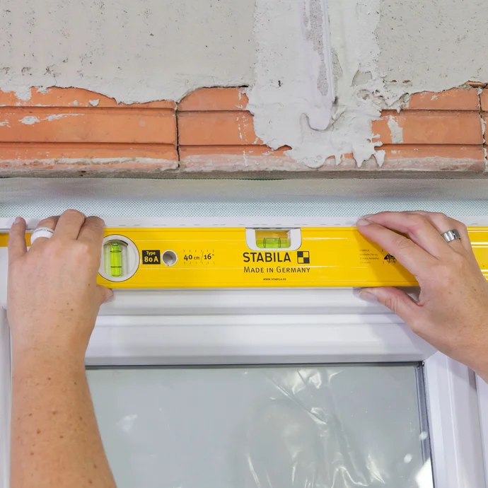 Ankleben der Anputzleiste im Sturzbereich des Fensters, ausgerichtet mit Wasserwaage