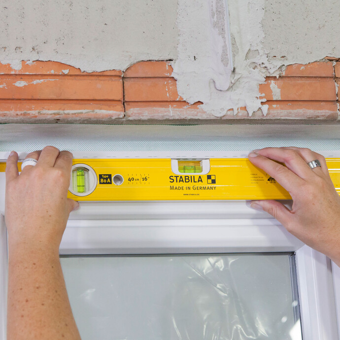 Ankleben der Anputzleiste im Sturzbereich des Fensters, ausgerichtet mit Wasserwaage