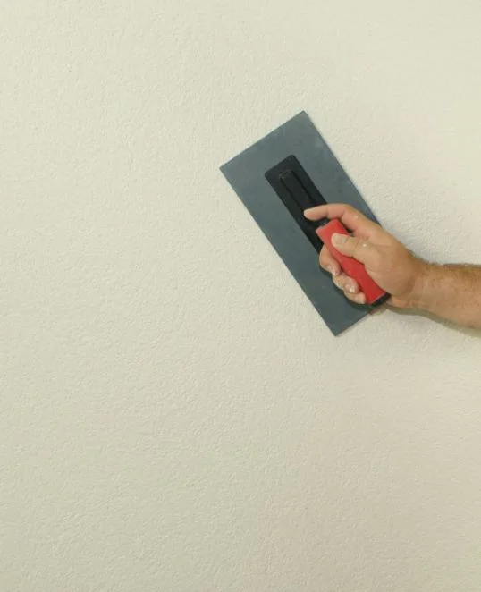 Un homme lisse un enduit blanc sur un mur à l’aide d’une truelle ; instructions étape par étape pour obtenir une surface murale parfaite.