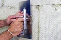 Hand glättet mit Kelle eine Fassade aus Dämmstoff, Schritt der Sanierung erklärt auf Baumit-Selbermachen.de.