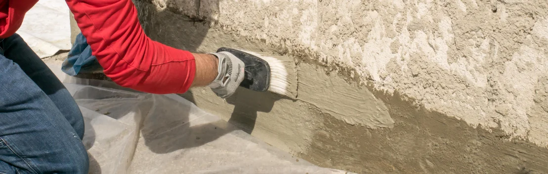 Un bricoleur applique du Mortier au pinceau sur un mur afin d&rsquo;obtenir une surface uniforme pour son projet de r&eacute;novation.