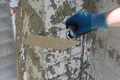 Hand trägt Putz mit Glättkelle auf Wand auf; DIY-Projekt mit Baumit-Produkten, ideal für Heimwerker beim Renovieren.