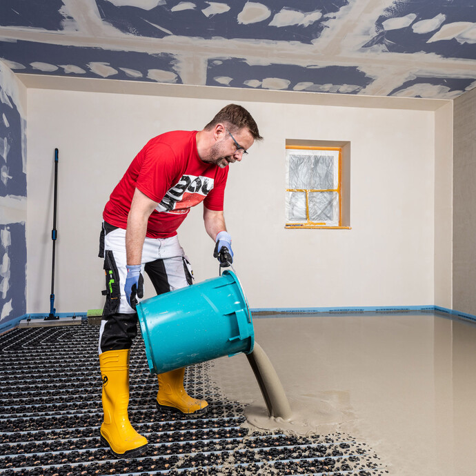 Mann leer die angerührte Nivelliermasse bzw. Ausgleichsmasse auf die eingebaute Fußbodenheizung.