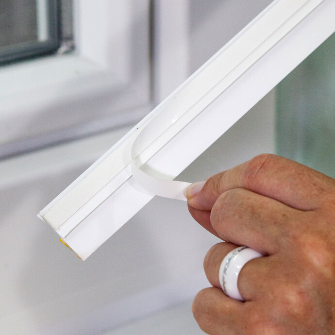 Detailfoto: Der Klebestreifen wird von der Rückseite der Anputzleiste abgezogen.