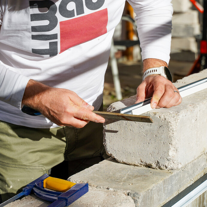 Handwerker feilt mit einer Eisenfeile die Schnittkanten des Abschlussprofils, um überstehende, scharfe Grate zu entfernen.