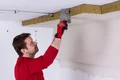 Die Baumit Kellerdecken-Dämmplatte aus Mineralwolle mit Vlies wird an die Decke geklebt.