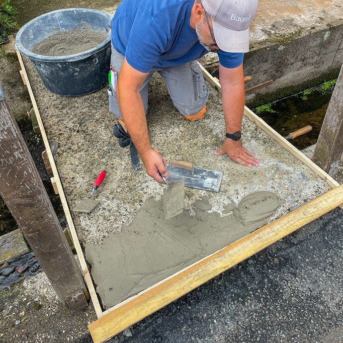 Handwerker trägt Gefällespachtel mit Glättkelle auf Betonfläche in Holzschalung auf.