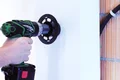 Heimwerker bohrt mit Bohrmaschine ein präzises Loch in eine weiße Wand für eine stabile Montage, Nahaufnahme.