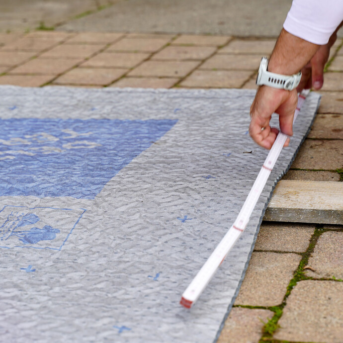Handwerker misst mit einem Meterstab die benötigten Teilstücke der Noppenbahn aus.
