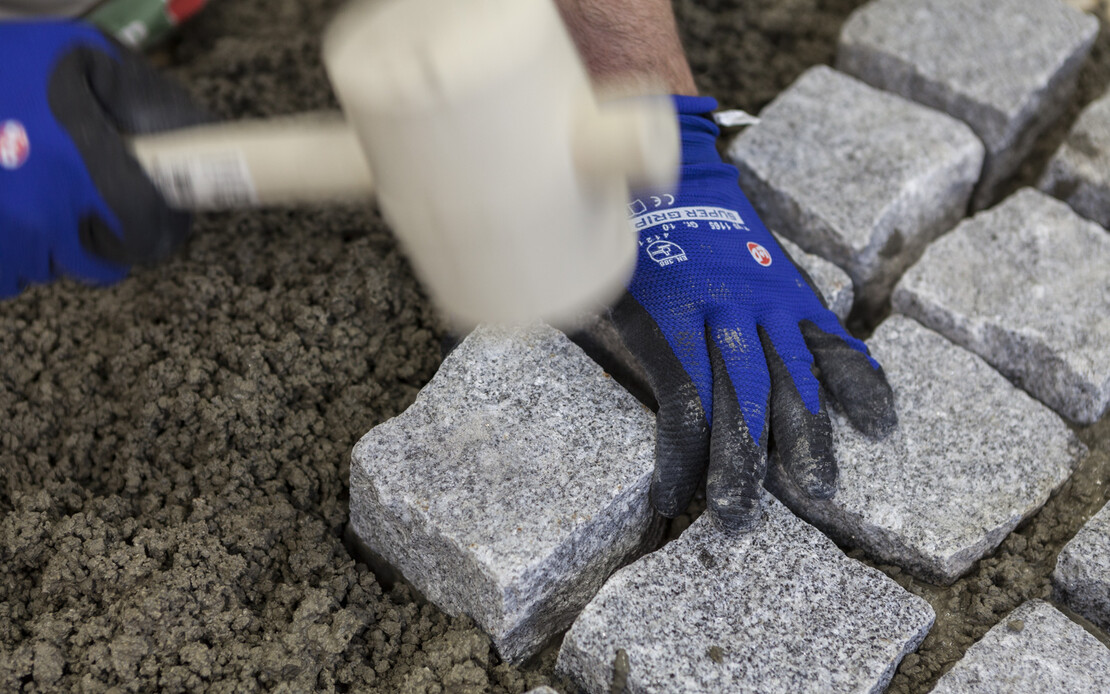 Granitpflasterstein mit Gummihammer in den frischen Pflasterdrainm&ouml;rtel einklopfen