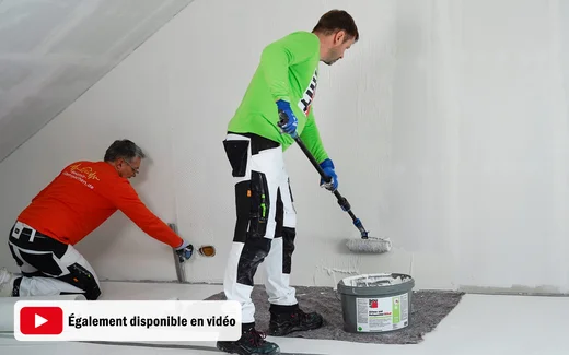 Deux hommes appliquent un enduit intérieur blanc sur le mur et la pente du toit dans le cadre d’un projet de rénovation.
