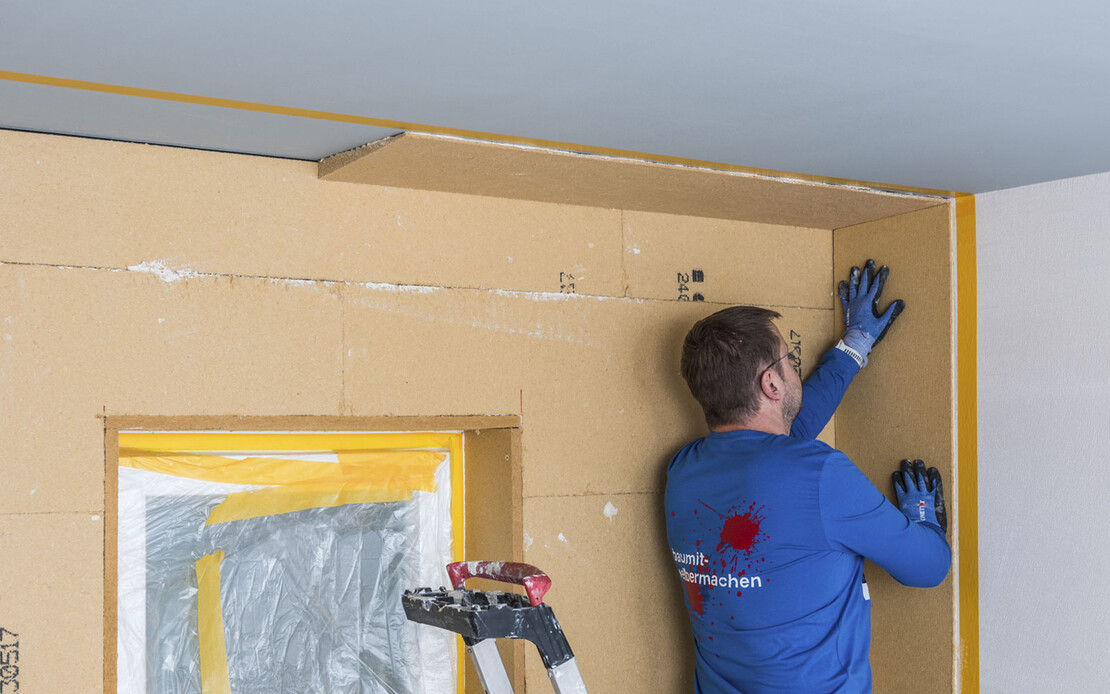 Die Innend&auml;mmung mit Holzfaserd&auml;mmplatten wird als geklebtes System verarbeitet. Hier wird gerade der Anschlusskeil an die Wand geklebt.