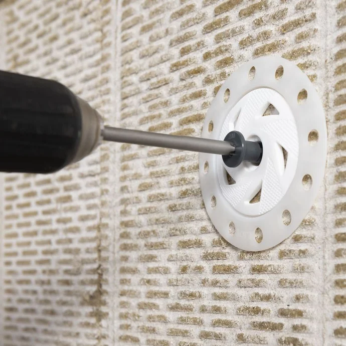 À l'aide d'une perceuse, on fixe un panneau isolant au mur à l'aide d'une cheville spéciale.