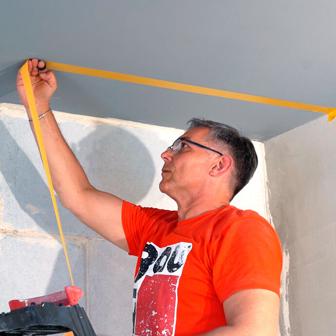Heimwerker klebt die Decke mit gelbem Klebeband ab.