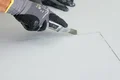 Heimwerker schneidet Gipskartonplatte mit Cuttermesser; Handschuhe sorgen für sicheren Halt und Schutz.