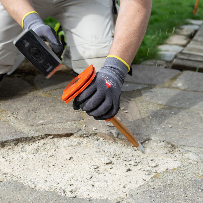 Mit Hammer und Meißel wird der Untergrund für das spätere Verkleben der Natursteinplatte vorbereitet.