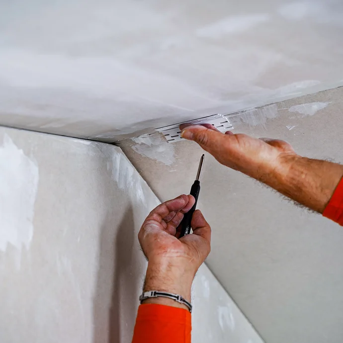 La surface de la construction sèche est marquée avec un morceau de profilé de joint de dilatation et un crayon.