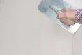 Hand beim Verputzen einer Wand mit einer Glättkelle, feiner Putz wird gleichmäßig aufgetragen.